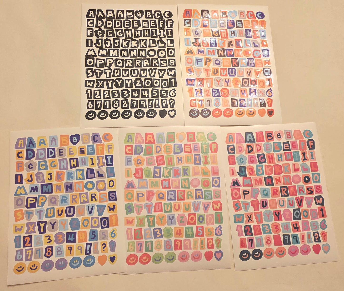 Four sheets of colorful alphabet and number stickers on a beige surface.