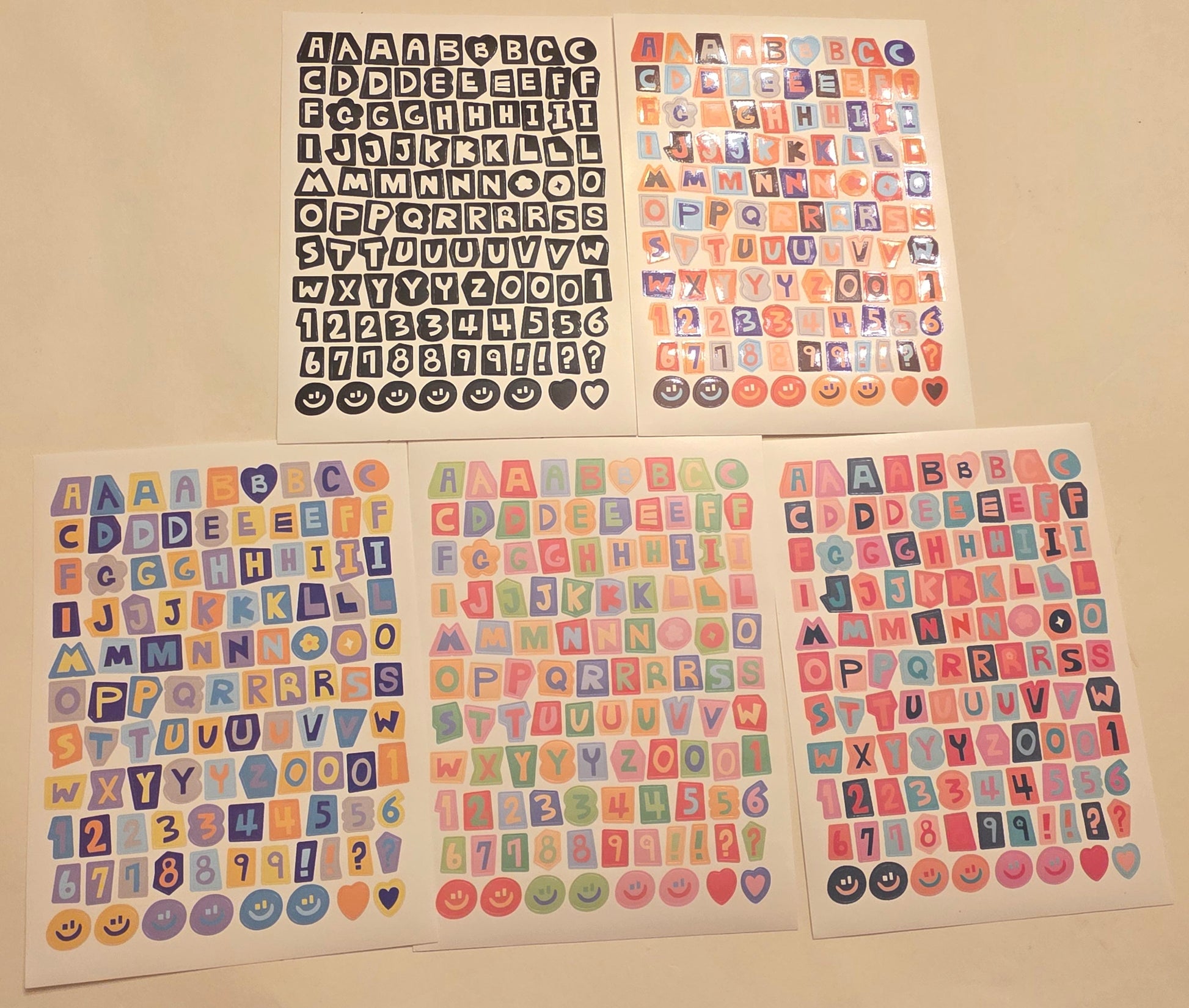 Four sheets of colorful alphabet and number stickers on a beige surface.