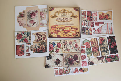 A flat-lay view of a Fissare Crafts 'Crimson Lusltre' collection of vintage scrapbooking papers, envelopes, and embellishments arranged on a white fabric background.