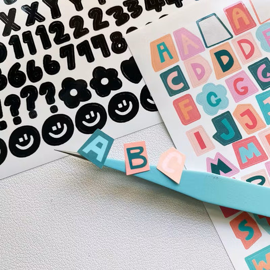 Sticker sheets with black numbers and symbols, colorful letters, and a blue tool on a white surface.