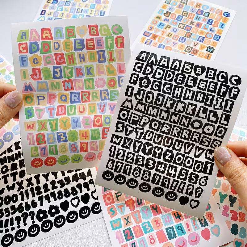 Collection of colorful and black letter, number, and emoji stickers held by a hand.